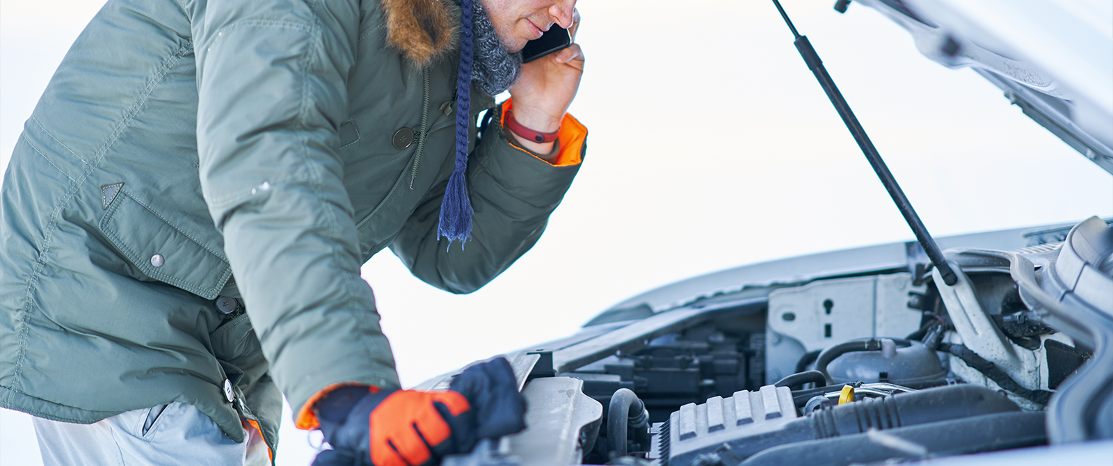 A man looking at his car engine in the snow