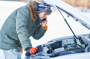 A man looking at his car engine in the snow