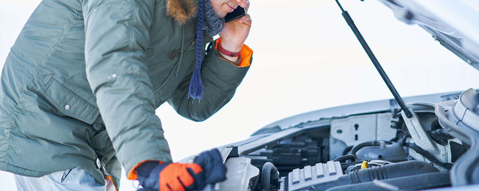 A man looking at his car engine in the snow