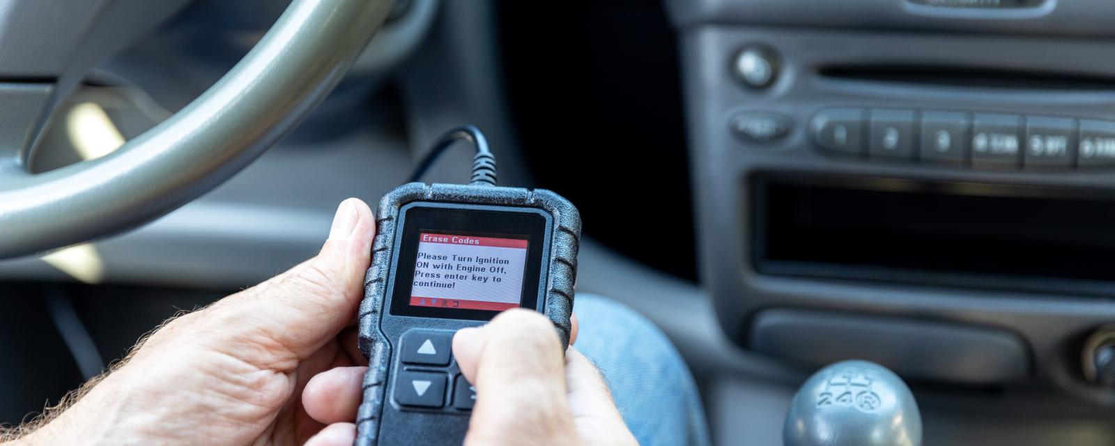 a man holding an obd-ii scanner in the driver's seat of a car