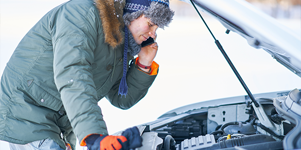 A man looking at his car engine in the snow
