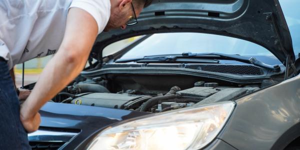 man bent over staring at a car engine
