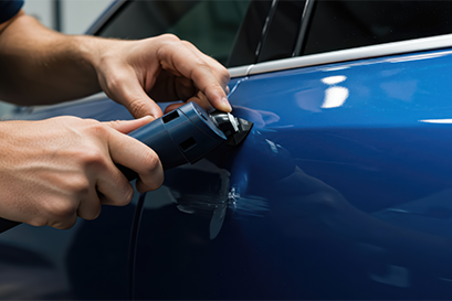 Auto mechanic using paintless dent repair tool on blue car door