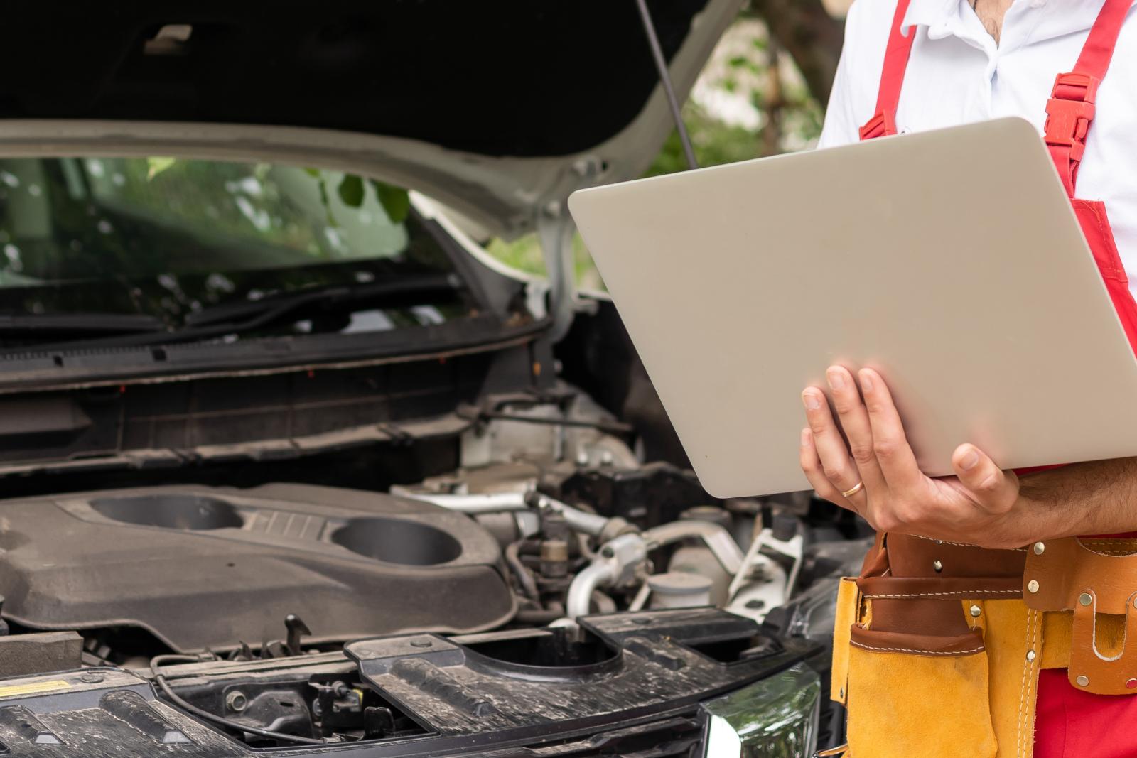 diyer holding laptop in front of car engine