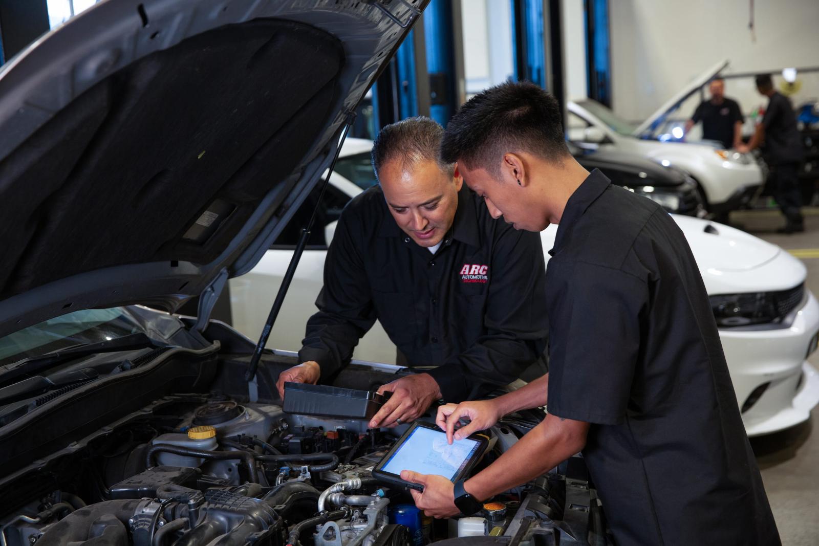 Two automotive shop employees working under the hood of a car