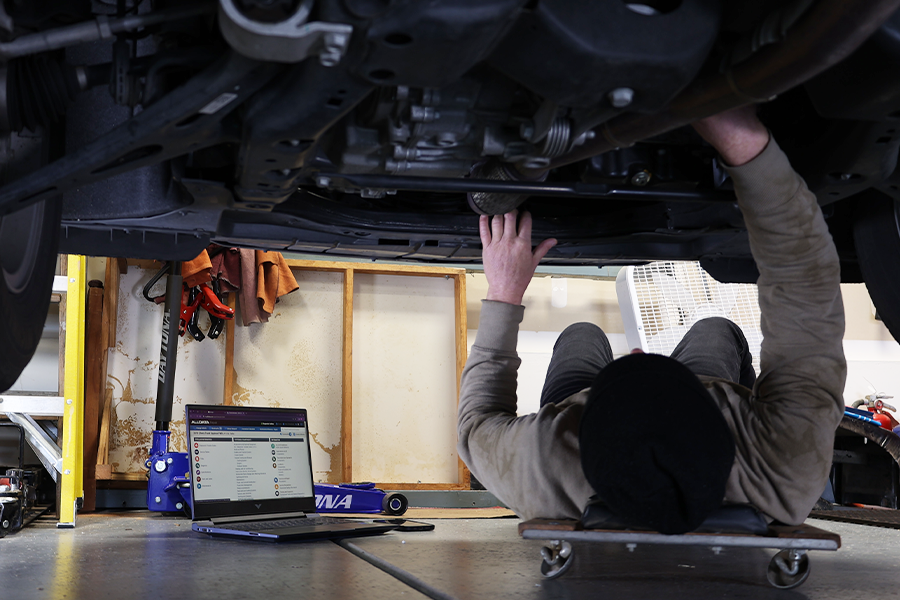 a man underneath a car with a laptop open to a car repair screen