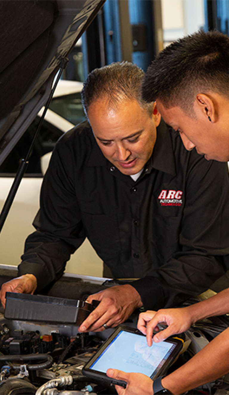 Techs looking at ALLDATA on a screen in front of a car