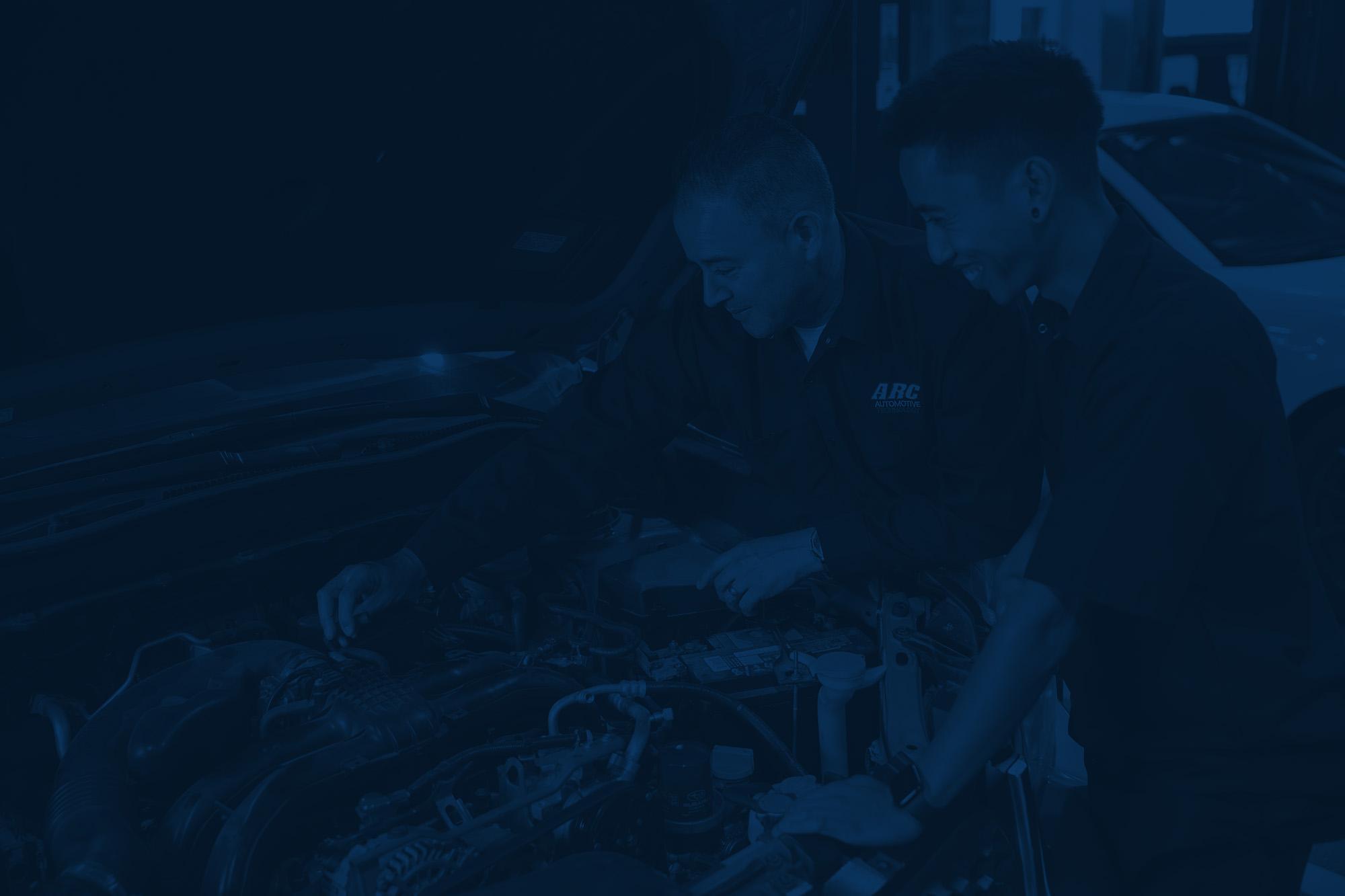 Two automotive shop employees working under the hood of a car