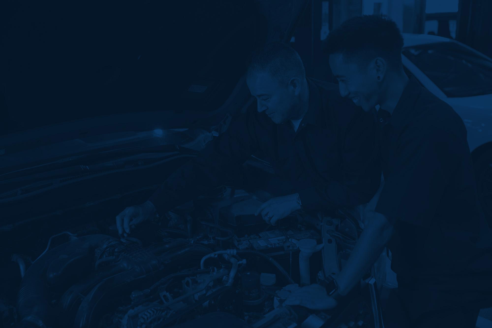 Two automotive shop employees working under the hood of a car
